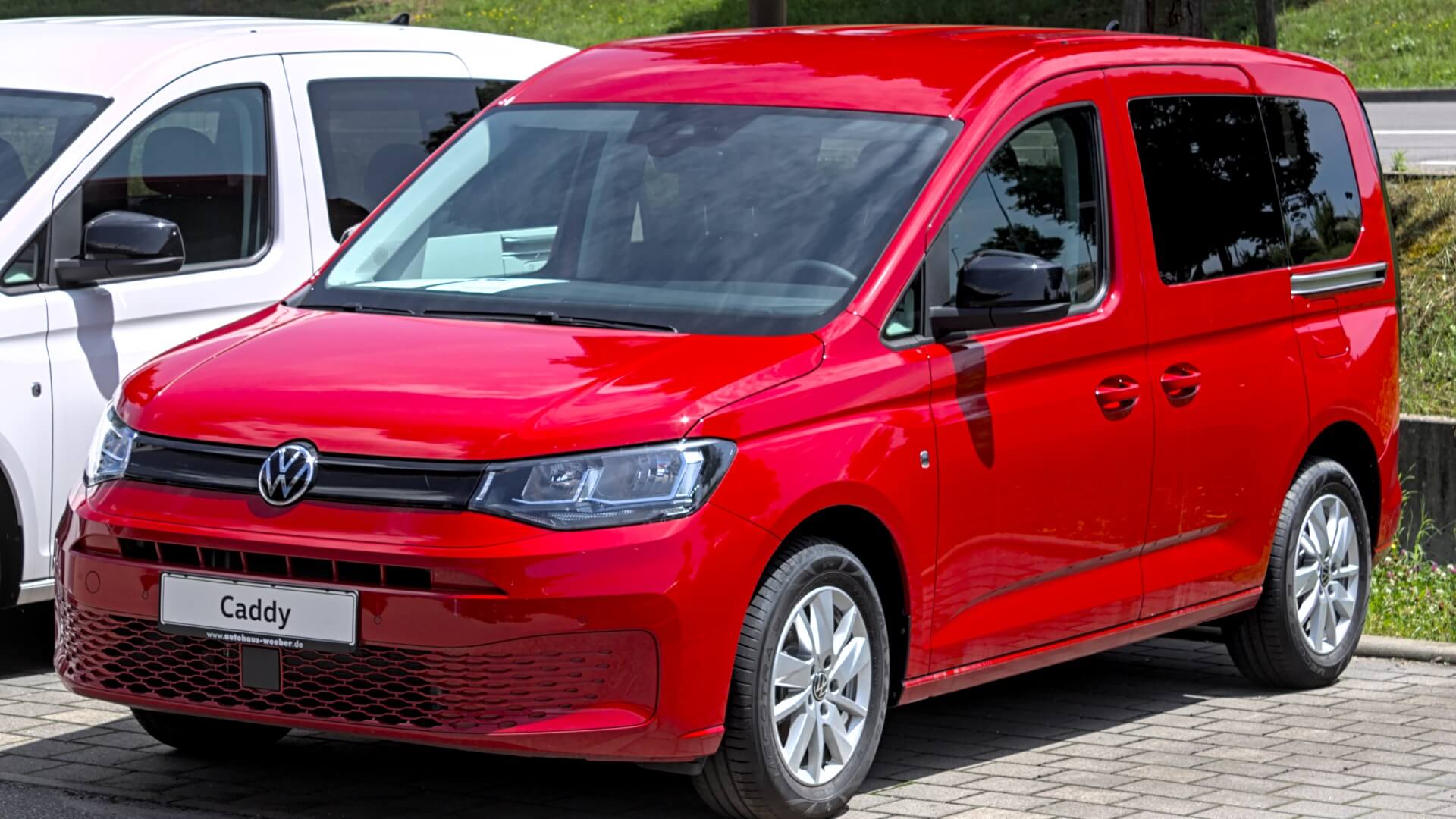 Photo of a brand new bright red VW Volkswagen Caddy van parked in a car park next to a similar white van