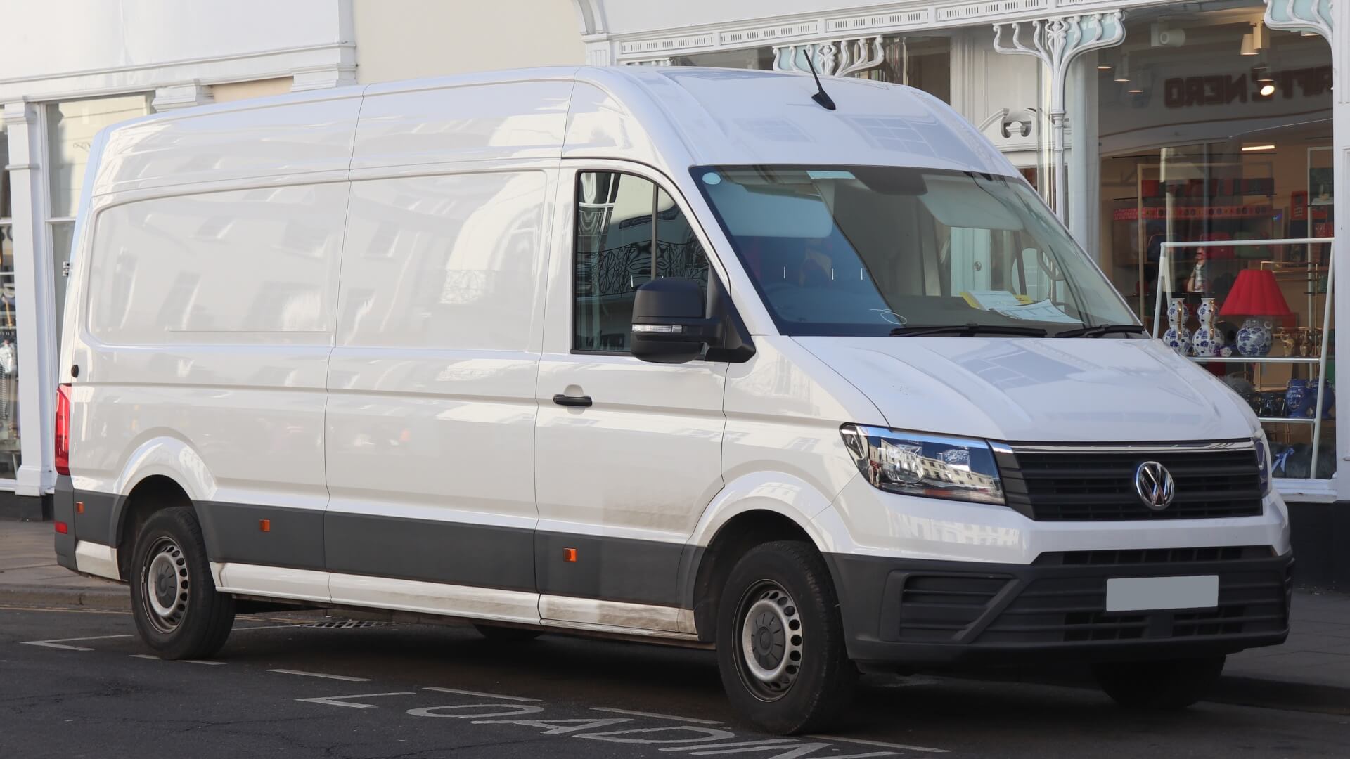 Photo of a white Volkswagen VW Crafter workman's van parked outside of a high street shop