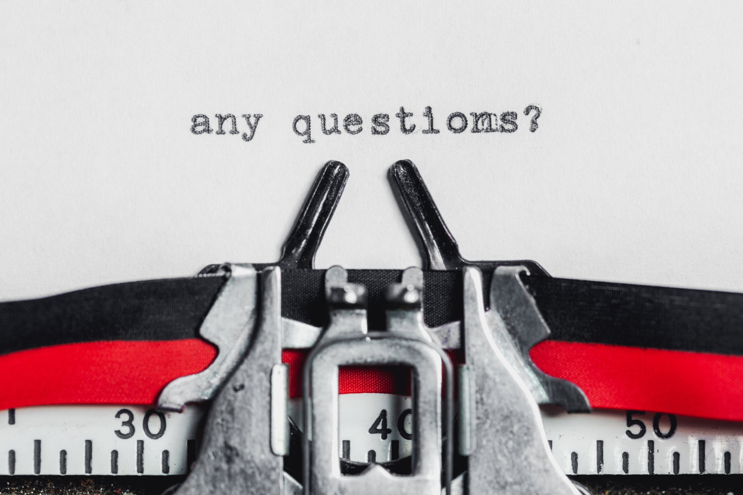 Photo of an old fashioned typewriter ribbon with the words "any questions?" in print on the white paper.