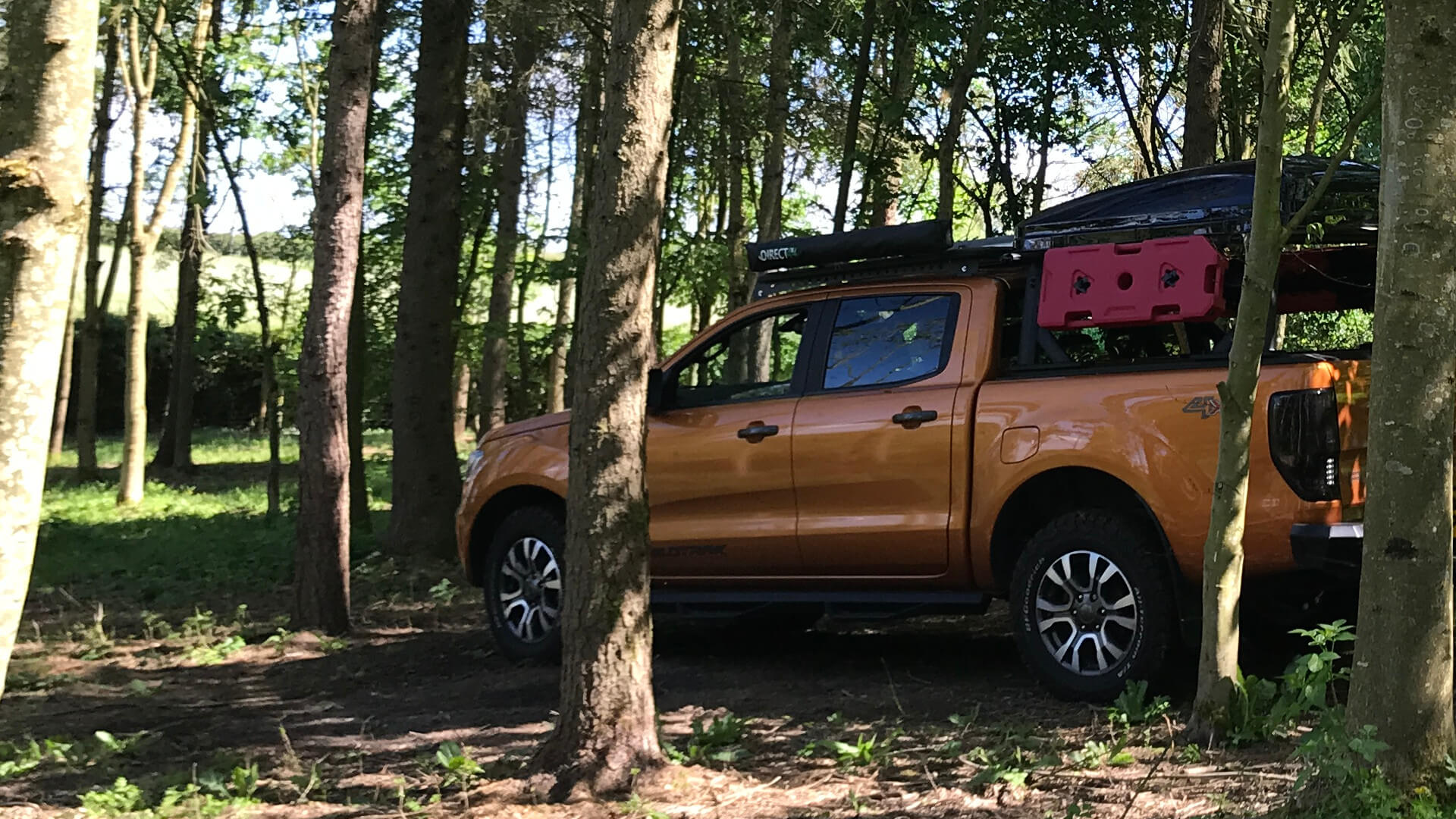 Direct4x4 Escapes expedition overland 4x4 vehicle hire rental service homepage link with an orange Ford Ranger Wildtrak equipped with camping gear in the forest nature