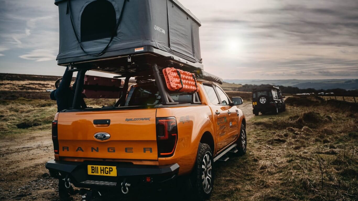 Direct4x4 Escapes expedition overland 4x4 vehicle hire rental service homepage link with an orange Ford Ranger Wildtrak equipped with camping gear in the forest nature