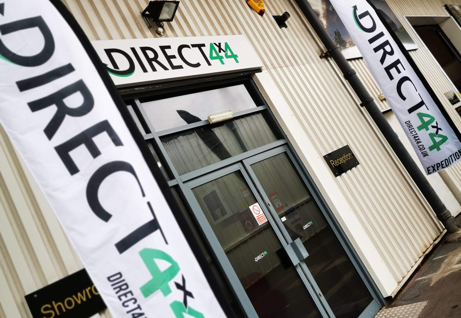 Direct4x4 Manufacturing Ltd. main front entrance double glass doors with stand-up flags on the pathway outside.