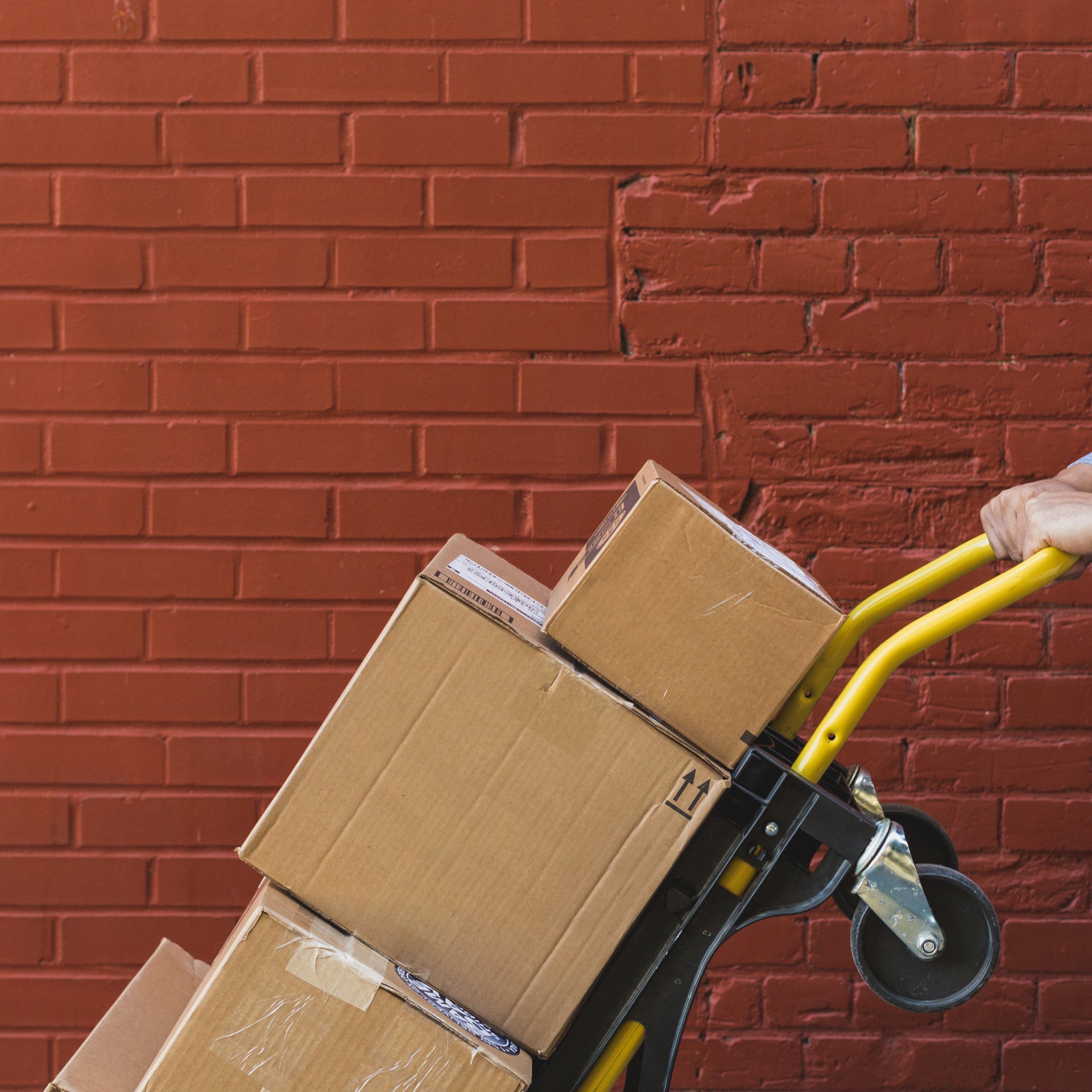 Direct4x4 free deliver and shipping service with a person pushing a trolley with multiple package boxes on in front of a brown brick wall