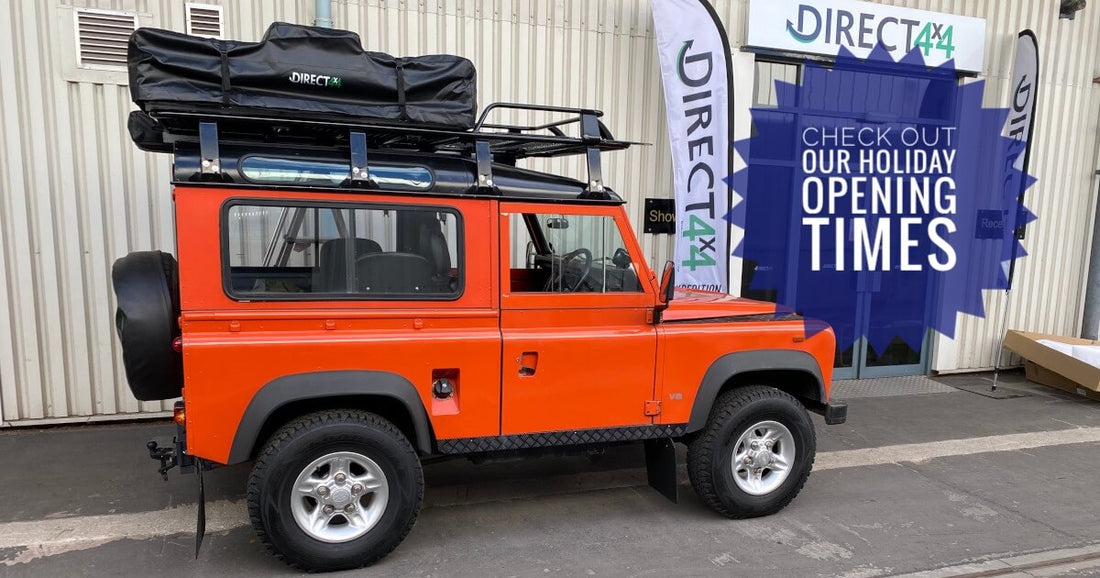 Land Rover Defender 90 in bright orange with expedition kit outside Direct4x4 offices with Holiday Opening Times badge