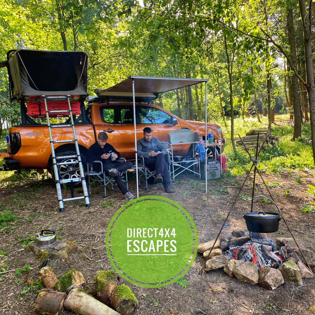 Direct4x4 Escapes camping out in a nature forest in the summer with an orange Ford Ranger Wildtrak with campfire, roof tent and side awning and camping expedition gear