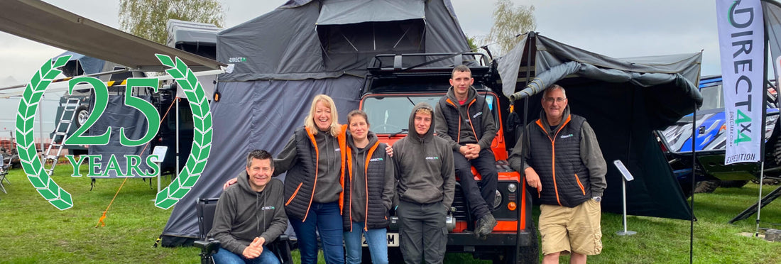 Direct4x4 team at the Land Rover Owners International Show in Peterborough in 2022 in front of a bright orange Defender 90 with roof top tent