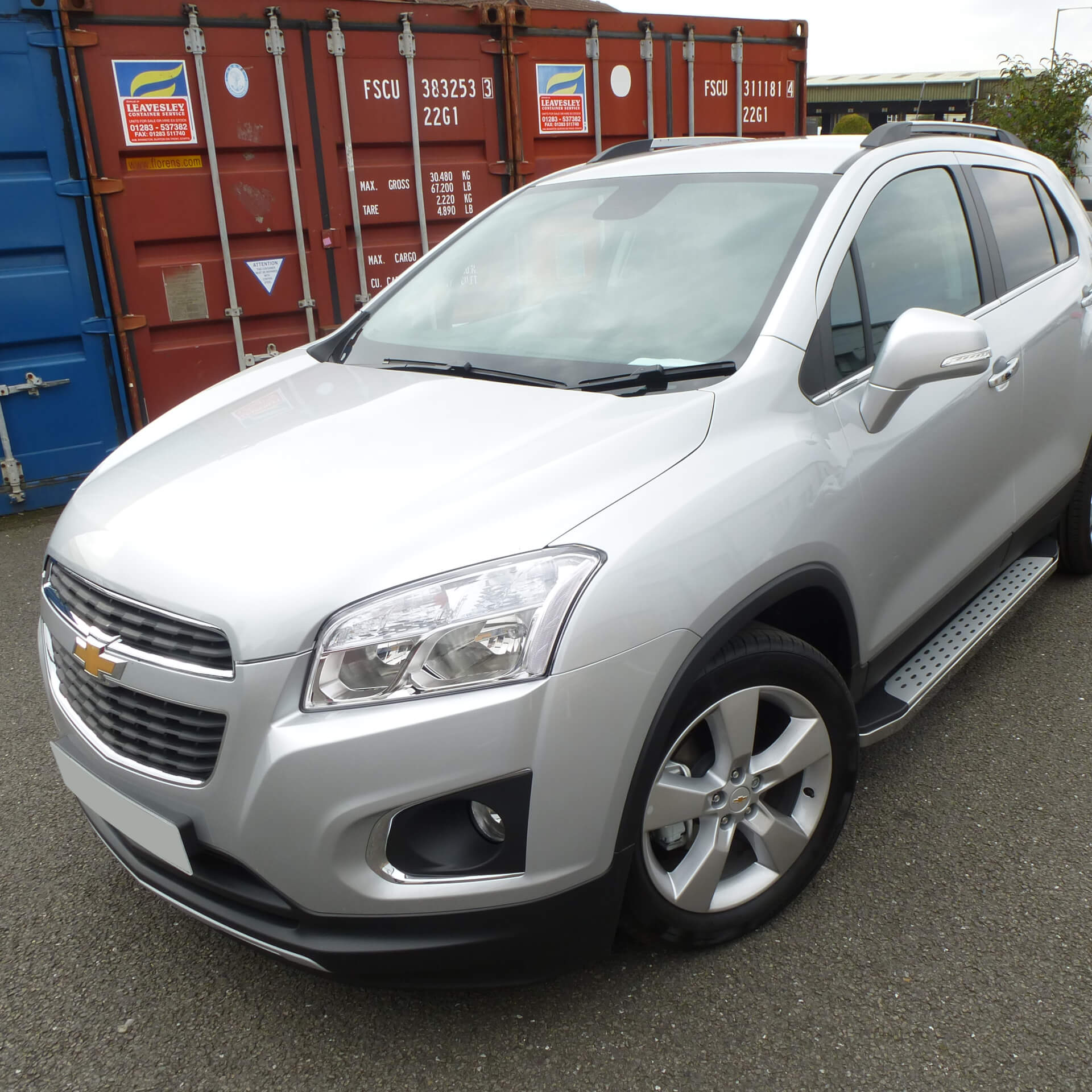 Direct4x4 accessories for Chevrolet Trax vehicles with a photo of a silver Chevrolet Trax with our freedom side steps fitted parked in front of shipping containers