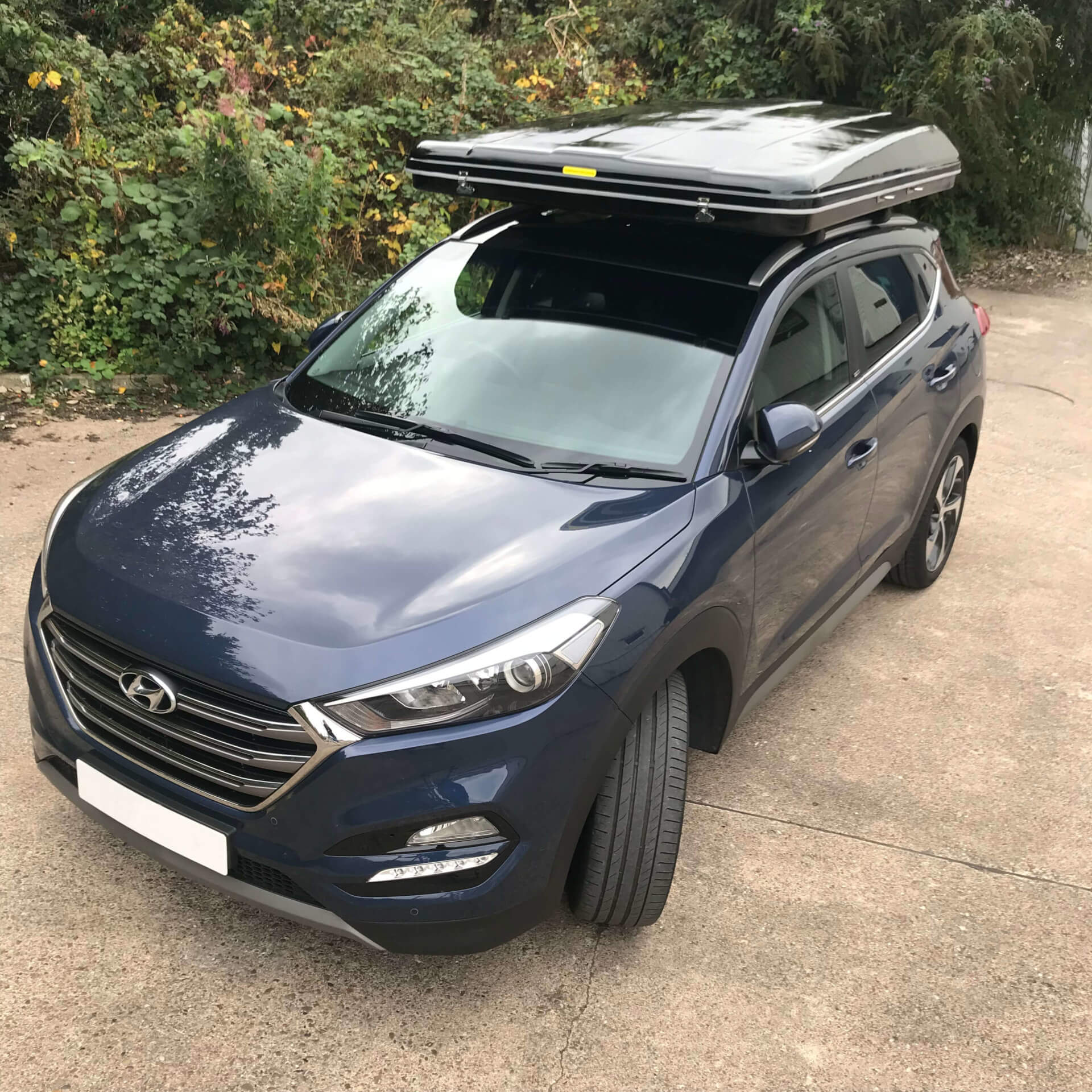 Direct4x4 accessories for Hyundai Tucson vehicles with a photo of a dark blue Hyundai Tucson parked up fitted with one of our hard shell roof tents on top