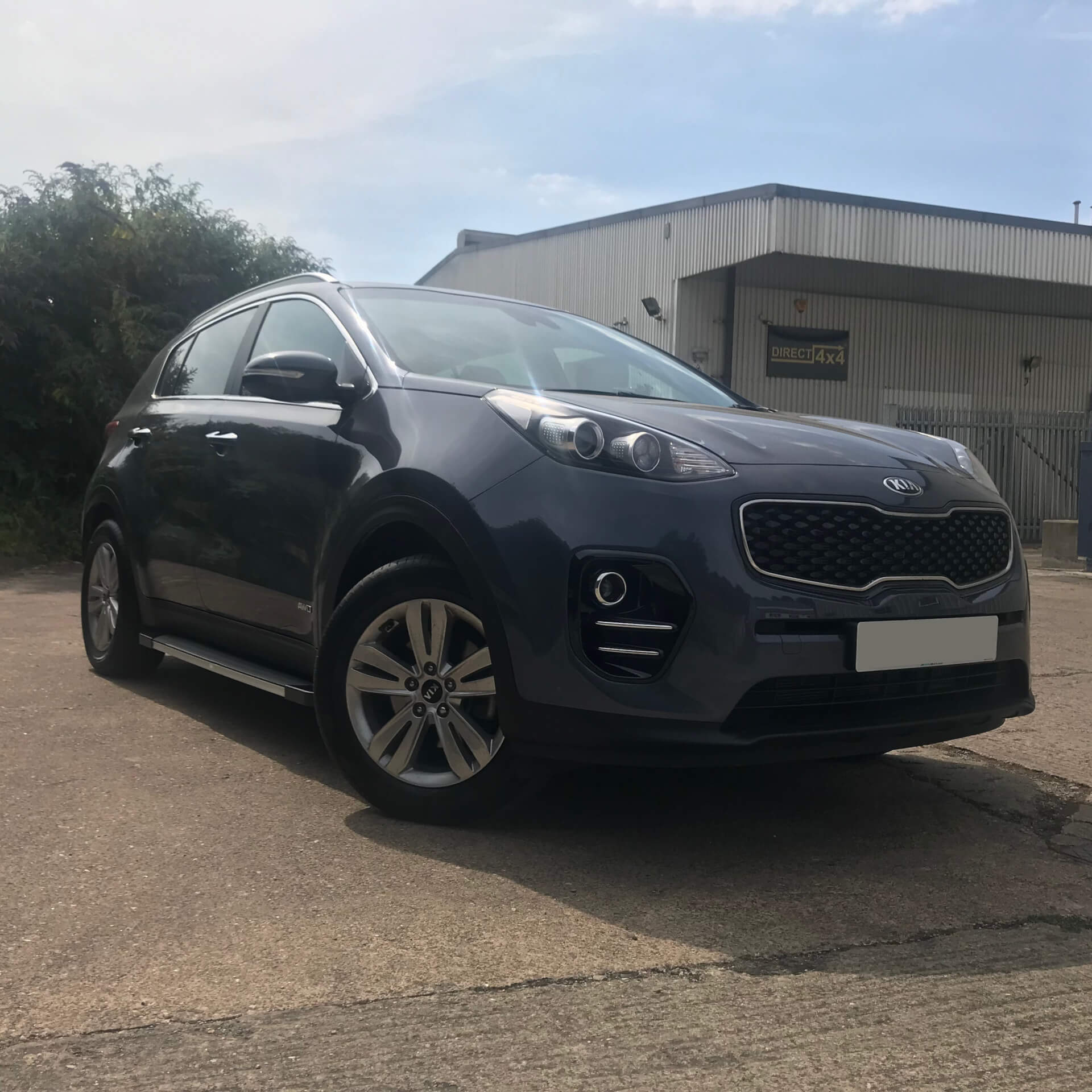 Direct4x4 accessories for Kia Sportage vehicles with a photo of a dark grey Kia Sportage fitted with side steps parked in the sunshine at out offices
