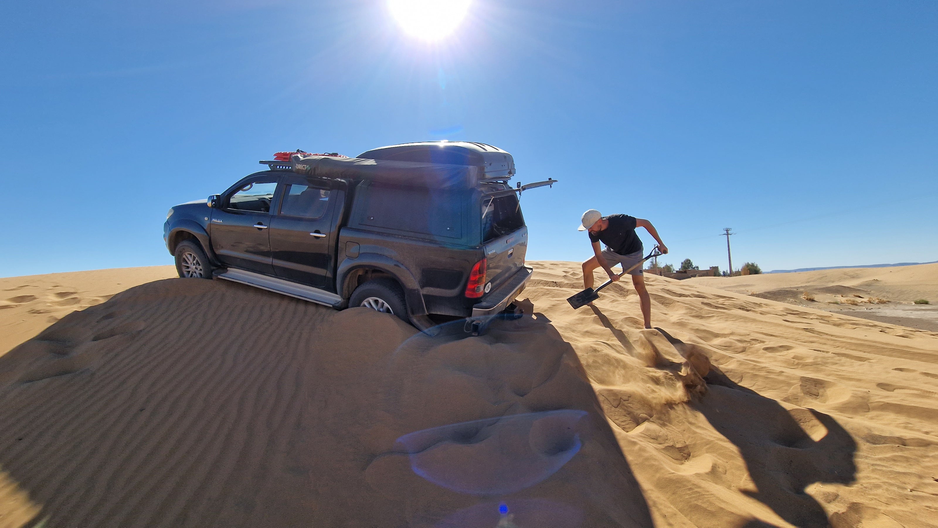 Photo of 2 people trying to dig out a Toyota Hilux pickup truck from the Moroccan desert.