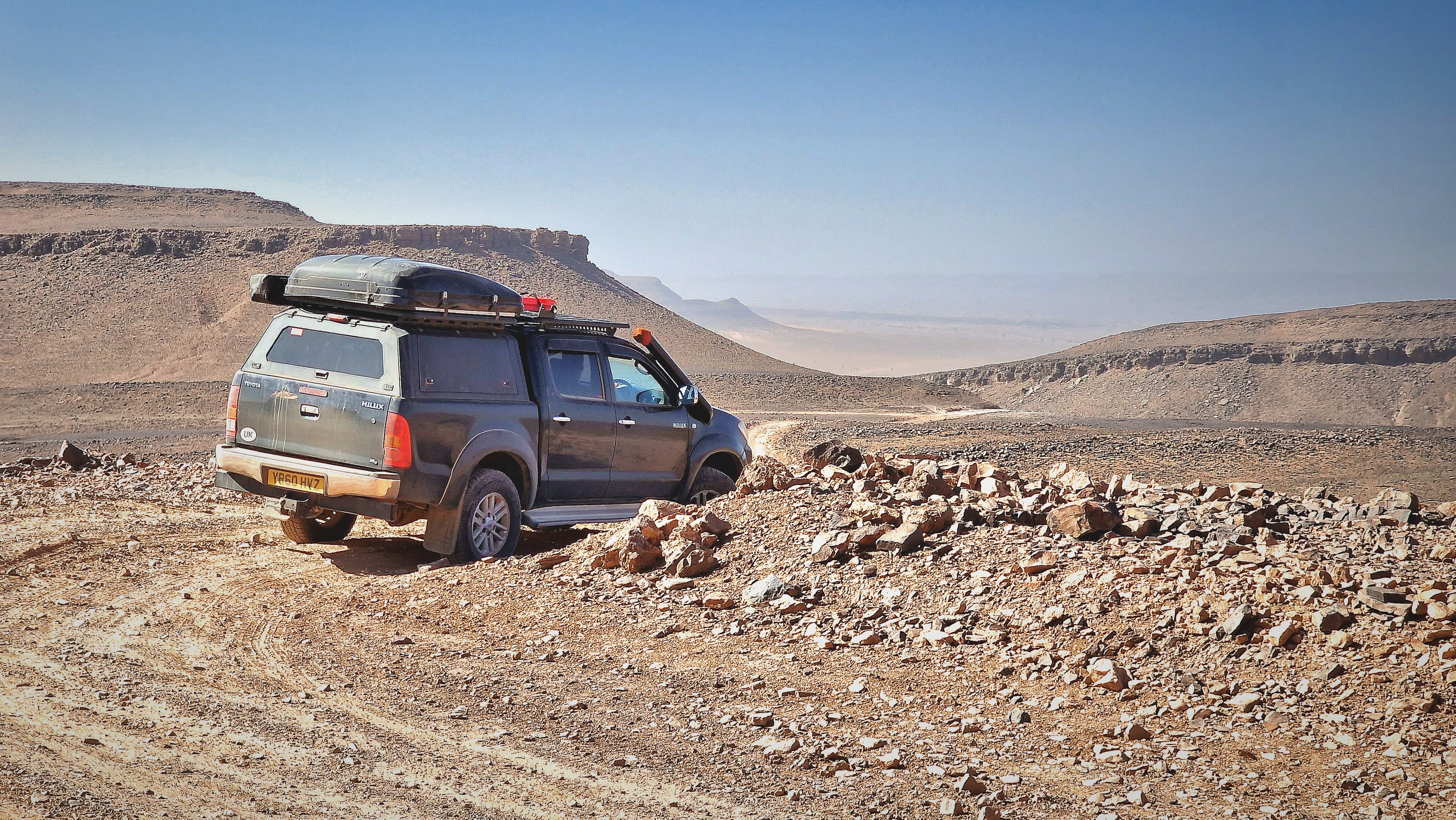 Photo of an expedition overland pickup truck off-roading in a pebbly hot Moroccan desert.
