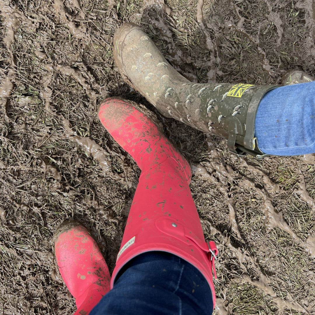 Photo of 2 pairs of wellington boots in a muddy field.