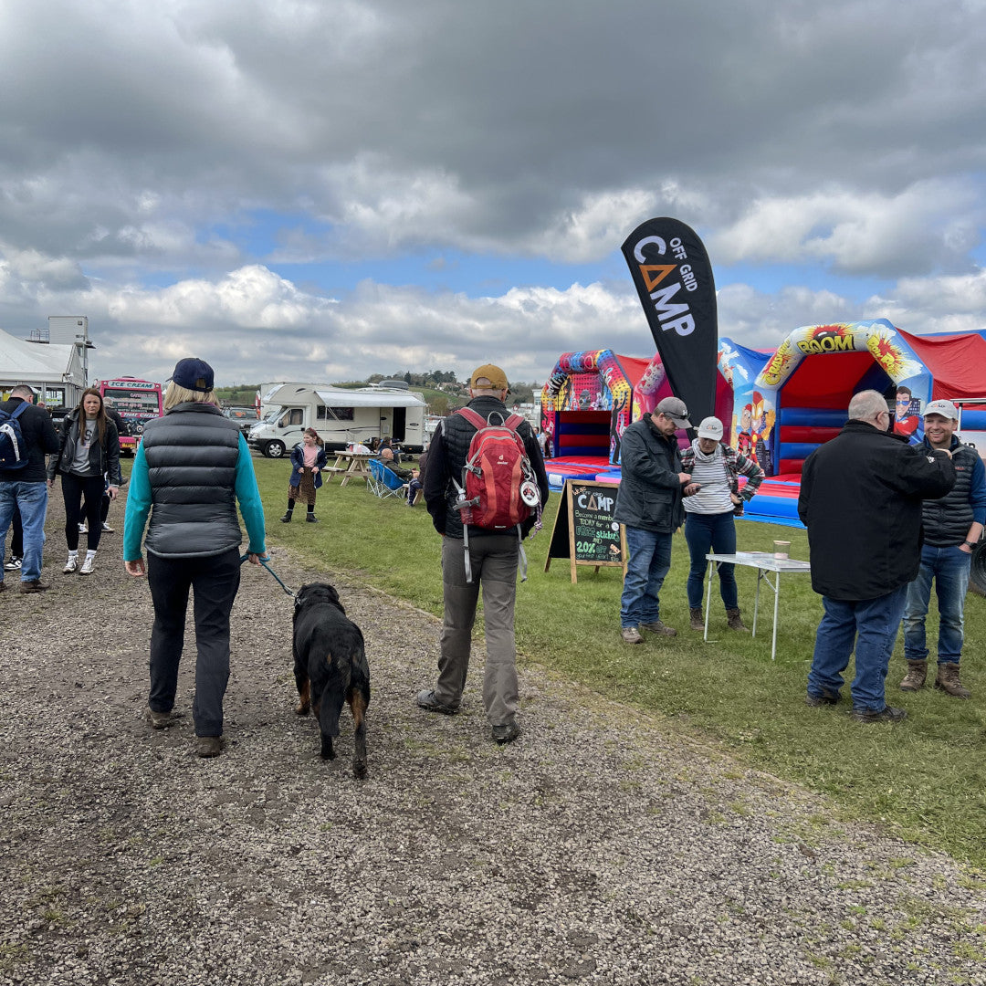 Photo of a small section of the Adventure Overland Show in Stratford-Upon-Avon 2023, including a bouncy castle and a person walking a black dog.