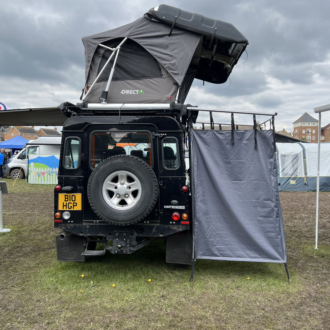 Photo of Land Rover Defender 110 with a Direct4x4 roof top tent fitted and an expedition overland camping privacy shower curtain awning in a field.