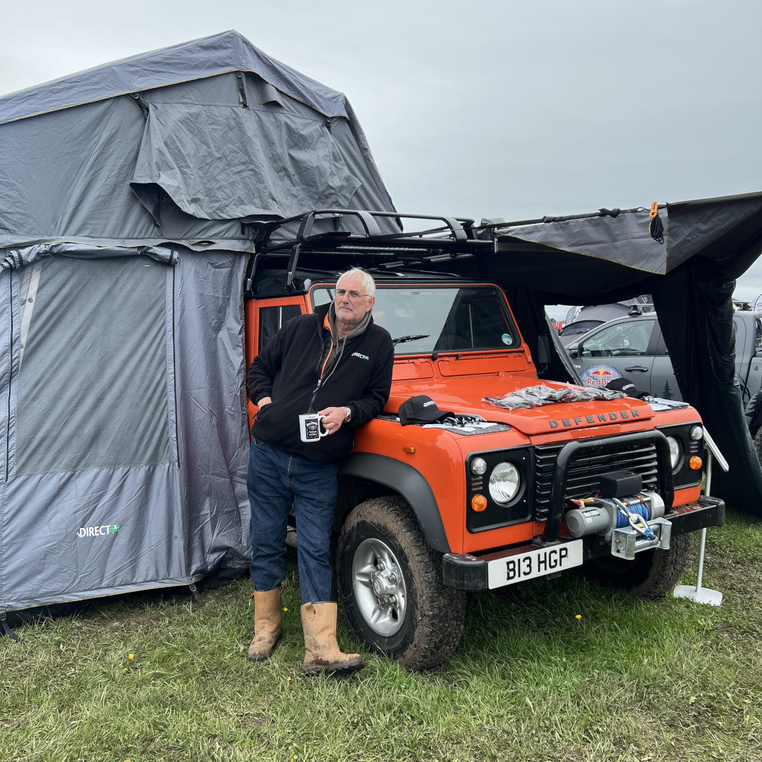A photo of a staff member leaning in front of the bright orange Land Rover Defender 90 from Direct4x4, kitted out with lots of overland expedition camping gear.