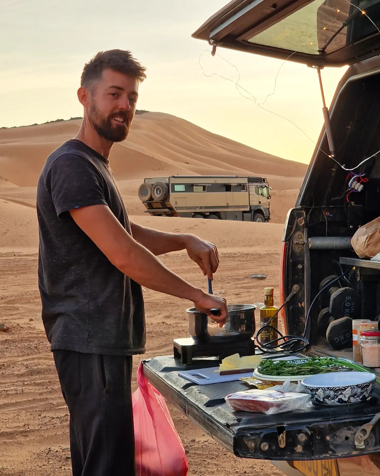 Photo of man cooking out the back of a pickup truck load bed tailgate in the evening in the Moroccan desert.