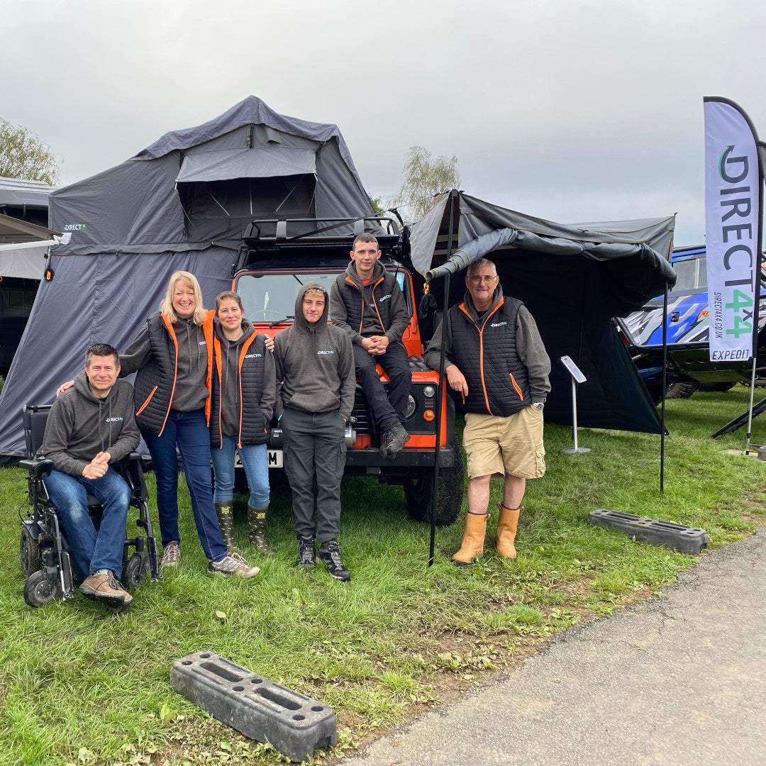 Photo of some members of the Direct4x4 staff with an orange Land Rover Defender 90 in the background fully kitted out with expedition overland camping gear 