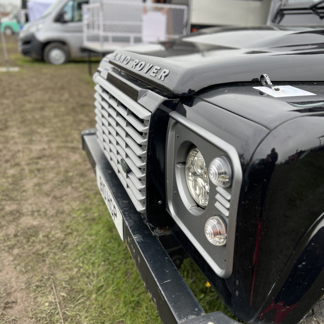 Close up photo of a front grille and logo of a black Land Rover Defender 110.