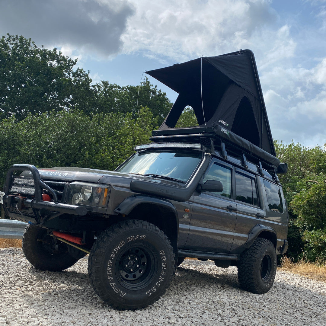 Photo of a rugged Land Rover Discovery 2 parked on some gravel with a roof top camping tent setup.
