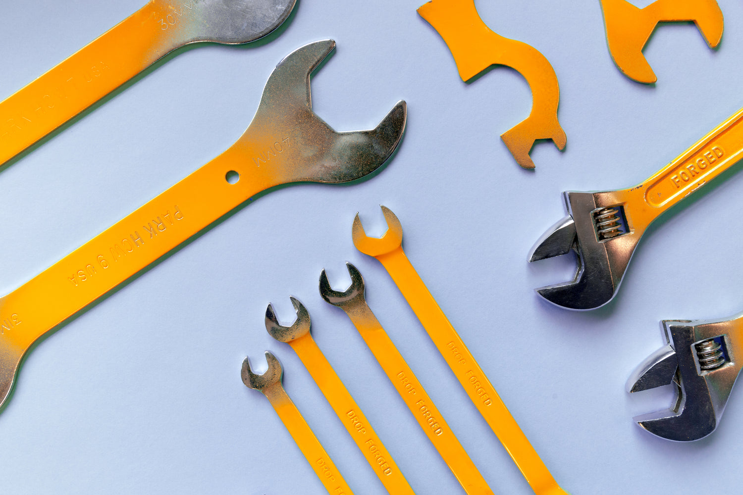 Photo of some yellow and siler wrenches and spanners on a light blue table background.