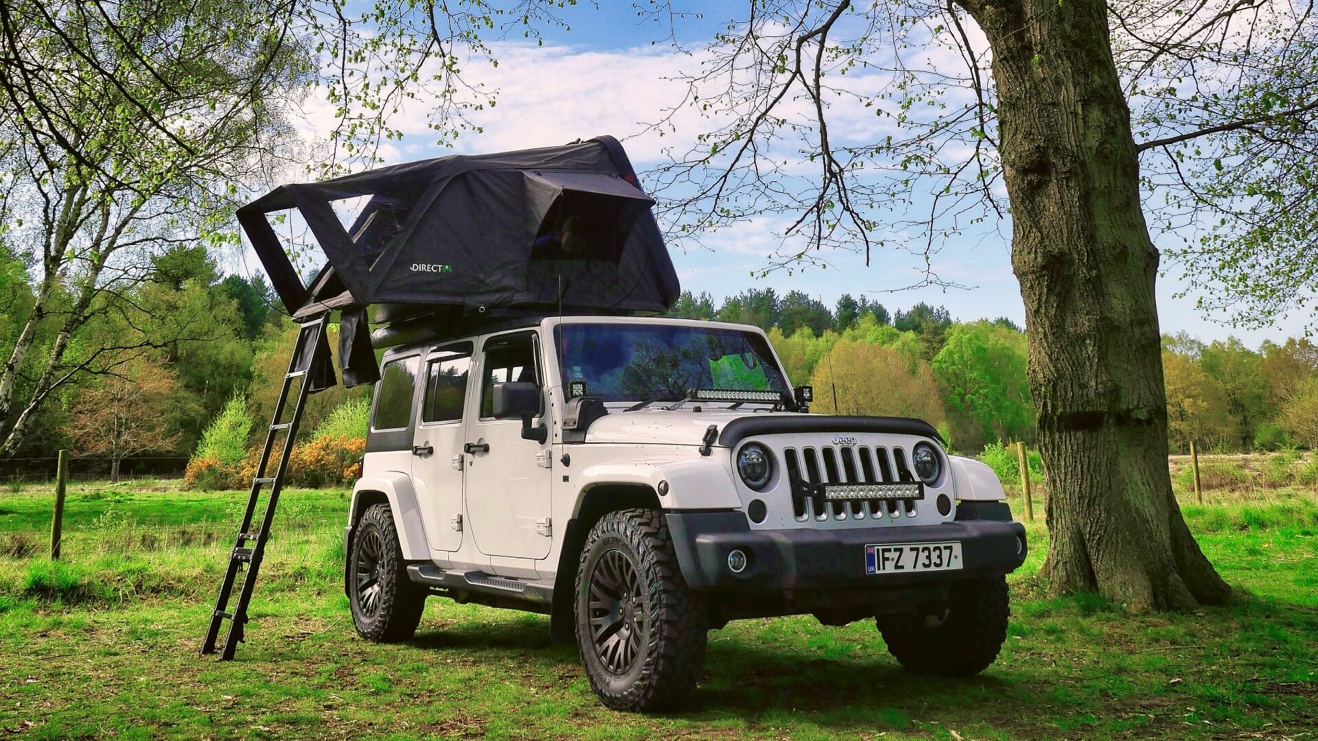 Photo of a white Jeep with a Direct4x4 roof top camping tent fitted parked in a green forest.