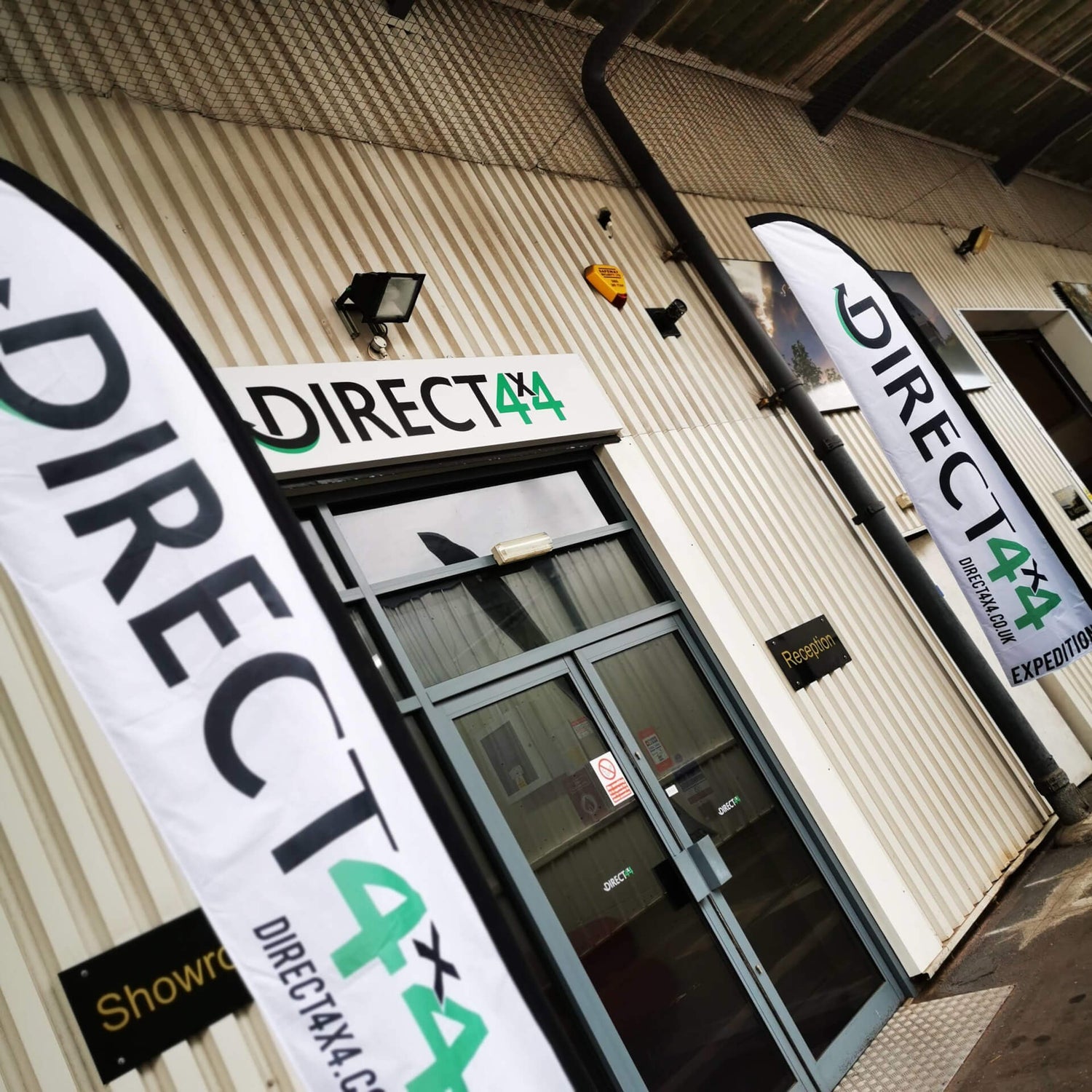 Direct4x4 Manufacturing Ltd. main front entrance double glass doors with stand-up flags on the pathway outside.