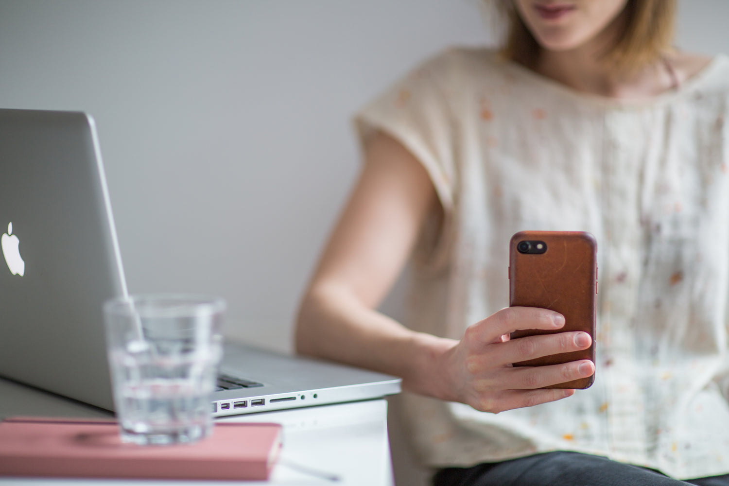 Photo of person holding a mobile phone next to an Apple Macbook on a table.